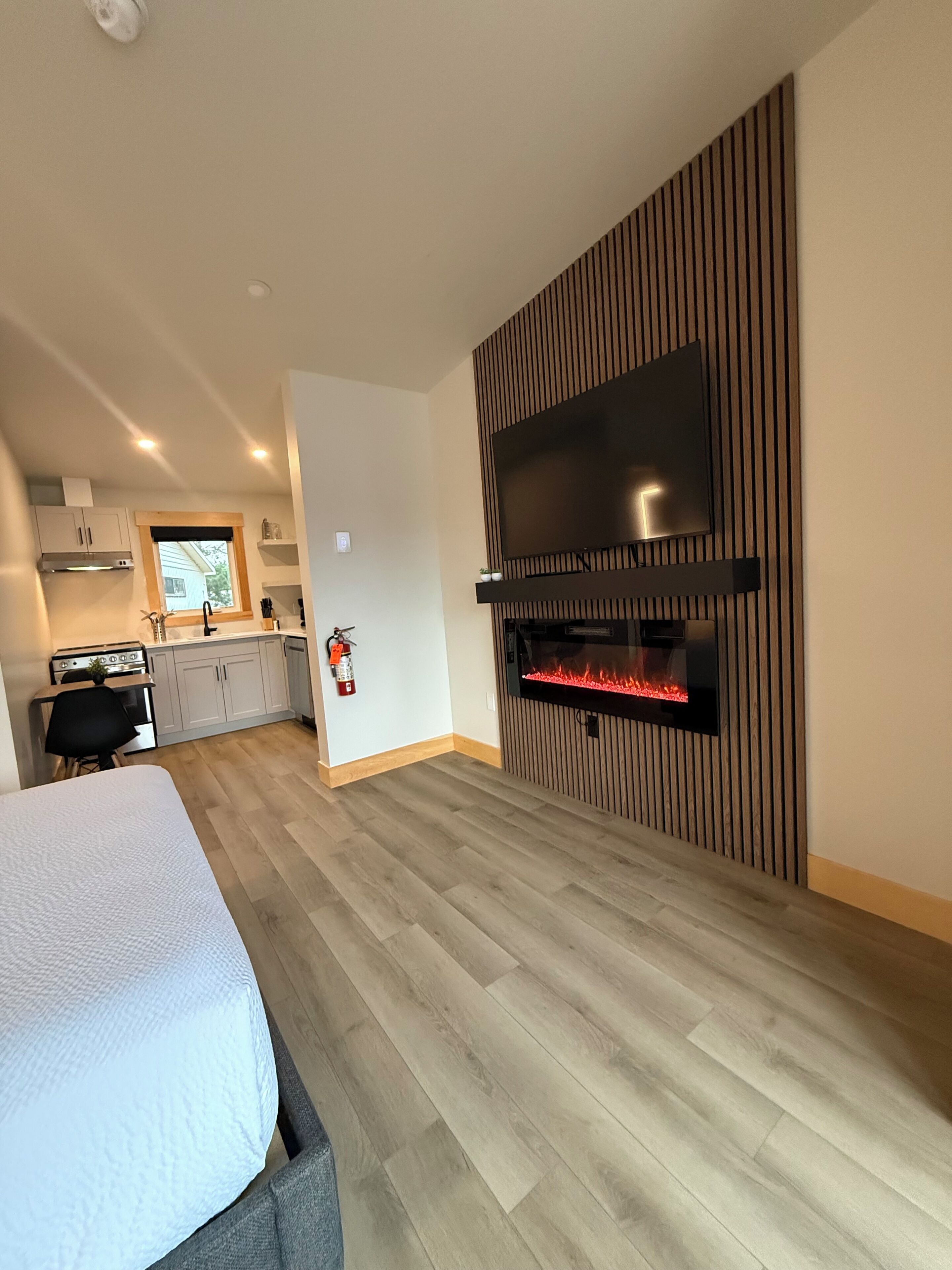 Una cocina moderna con estufa integrada, una zona de comedor con mesa y sillas, y una sala de estar con chimenea y un televisor grande montado en una pared de madera.