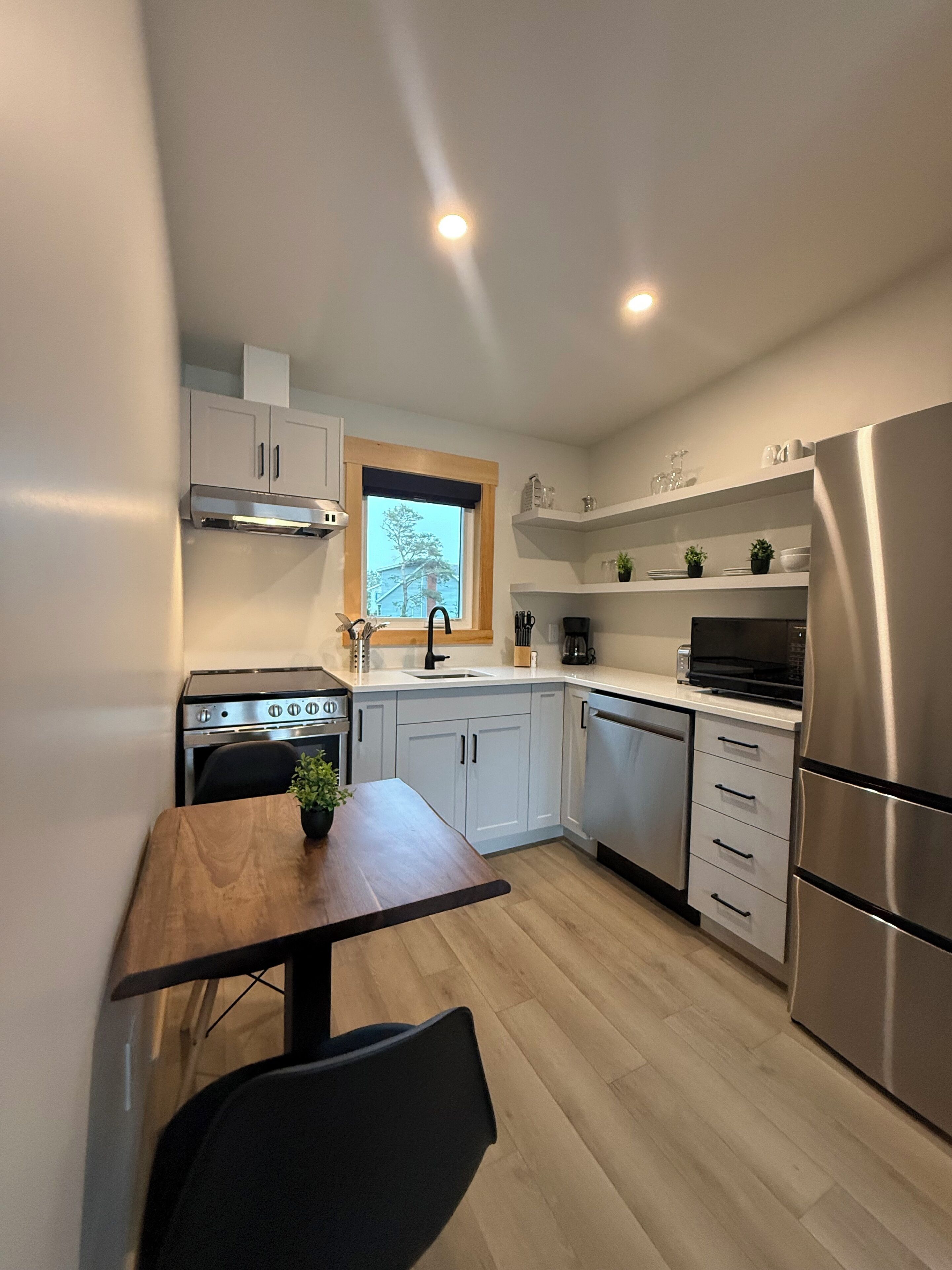 A modern kitchen with white cabinets, a stainless steel refrigerator, and a wooden dining table.