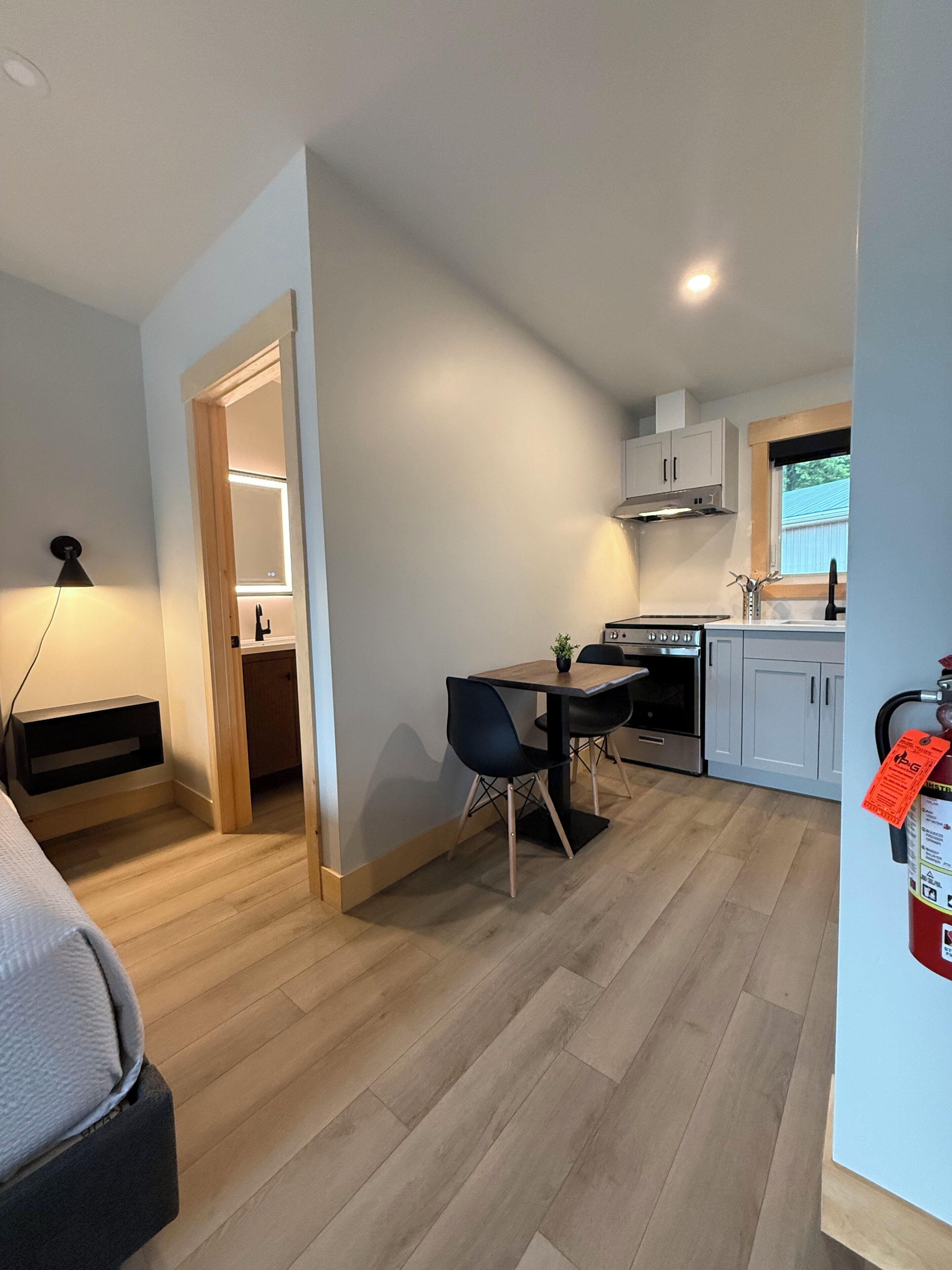 Une cuisine compacte dotée d’appareils électroménagers modernes, un coin repas avec une table et des chaises, et un extincteur visible.