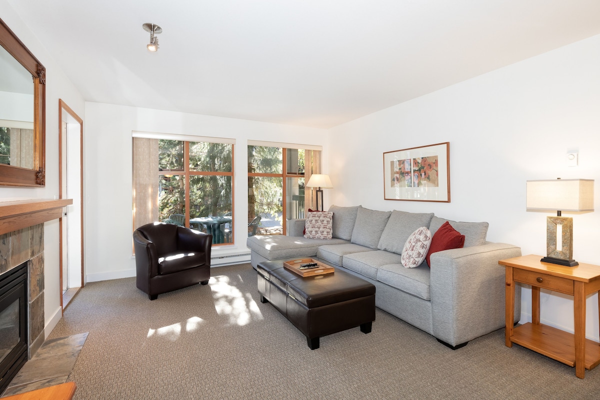 A modern living room with a fireplace, a grey sofa, a leather armchair, and a wooden side table.