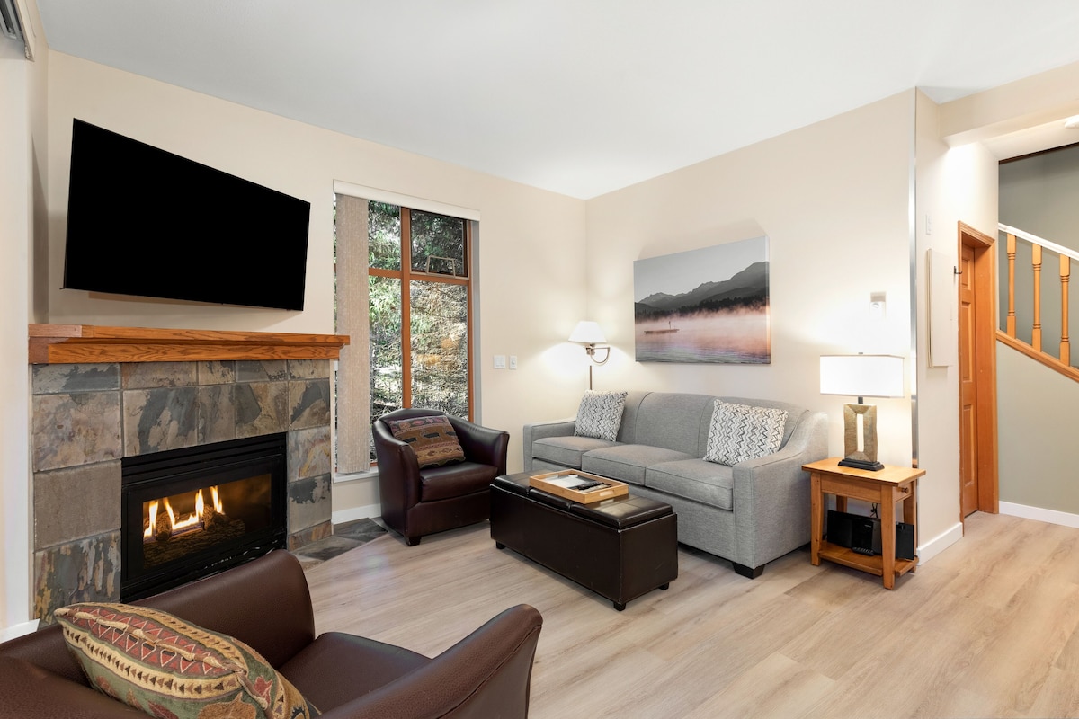 A living room with a fireplace, a flat-screen TV, a sofa, a coffee table, and a lamp.