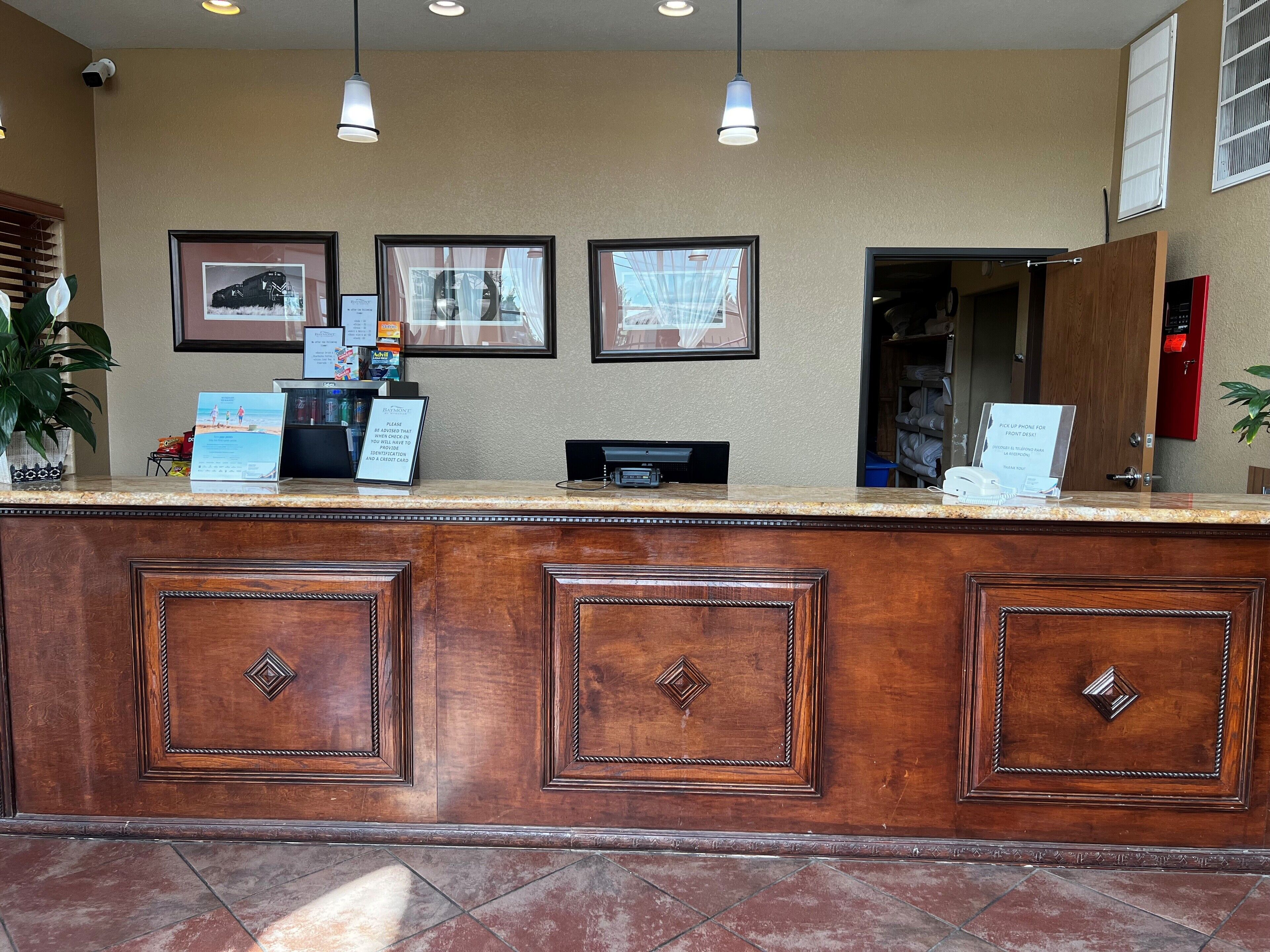 A reception desk with framed pictures on the wall, a plant, and a sign advising to pick up a phone for front desk.