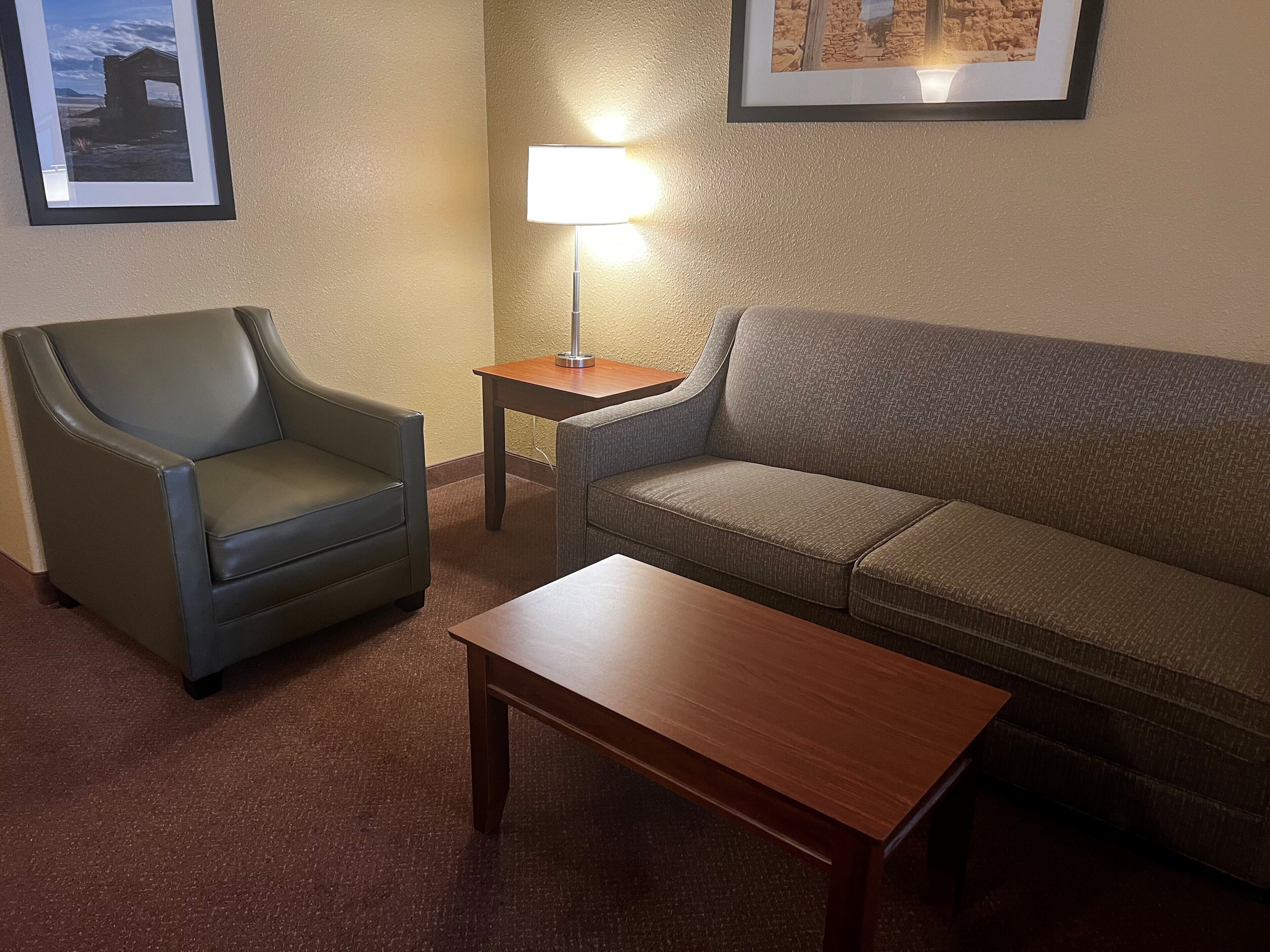 Una habitación con un sillón de cuero, un sofá y una mesa de centro de madera. Hay una lámpara en una mesita auxiliar y cuadros en la pared.