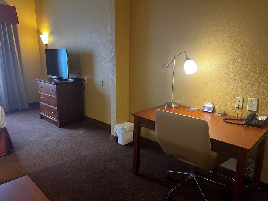 Ett hotellrum med ett skrivbord i trä, en stol, en bordslampa, en telefon och en tv som står på en byrå.