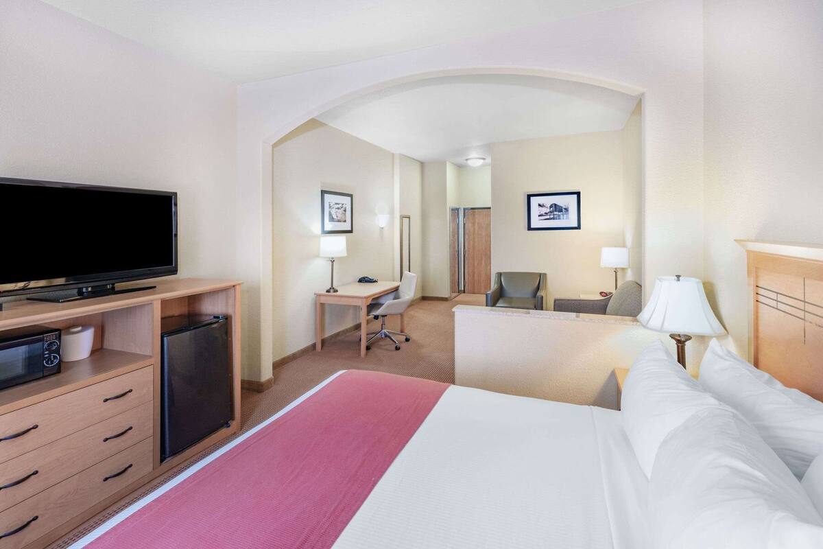 Une chambre d’hôtel équipée d’un lit, d’un bureau, d’une chaise, d’une télévision et d’un petit réfrigérateur.