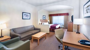 Quarto de hotel com sofá, mesinha, escrivaninha com telefone, cadeira e cama com cabeceira vermelha.