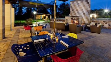 An outdoor patio with a table set for dining, surrounded by wicker furniture and colorful chairs.