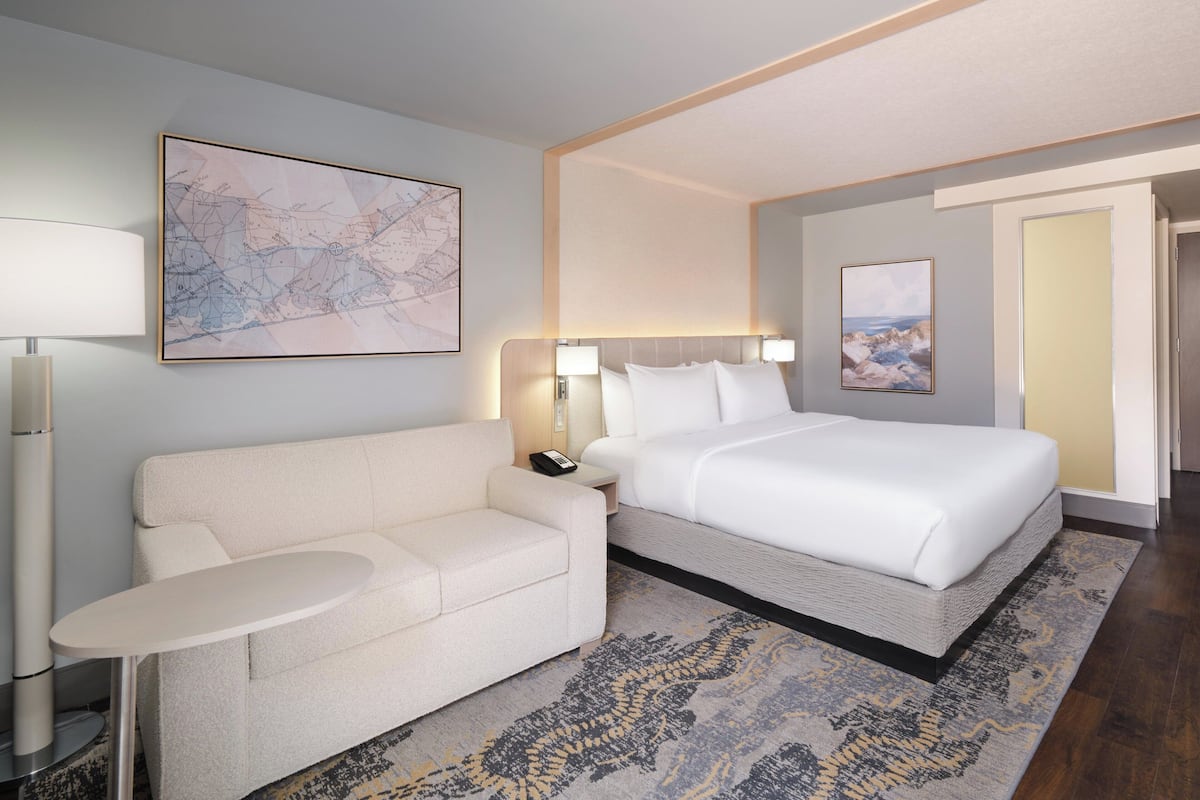 A hotel room with a bed, a sofa, a small table, and a large abstract painting on the wall.