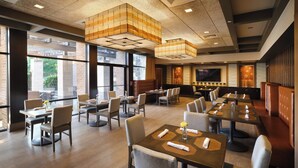 A restaurant with multiple tables and booths, large windows, and a modern ceiling design. - Hotel Indigo Long Island - East End by IHG (Riverhead)