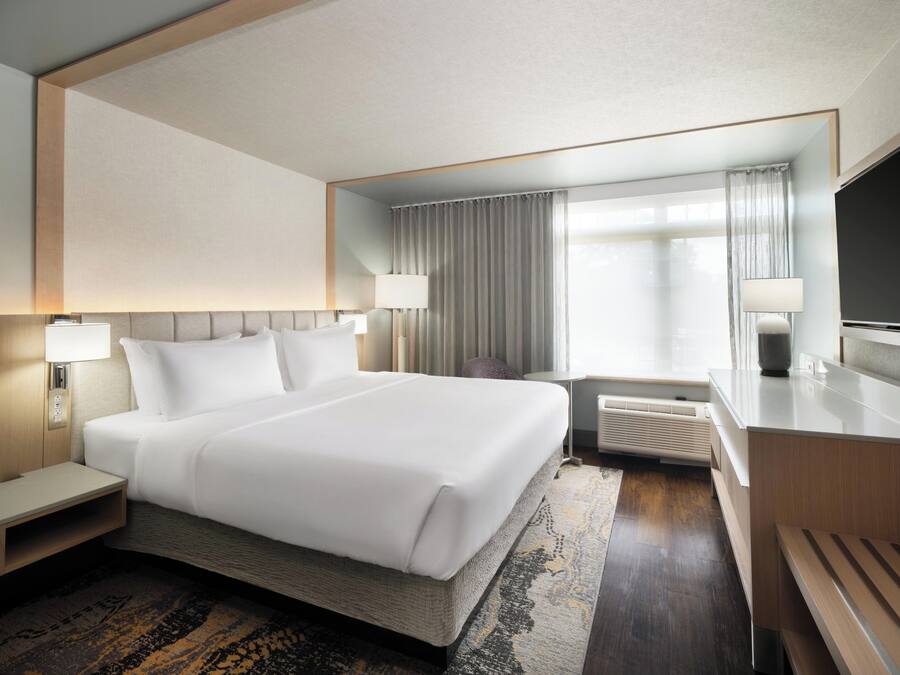 A hotel room with a large bed, bedside tables, a desk, a TV, and a window with curtains.