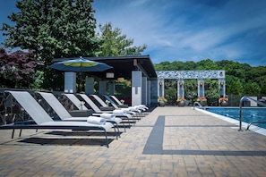 A poolside area with lounge chairs and umbrellas, a covered seating area, and a pool with a tiled deck. - Hotel Indigo Long Island - East End by IHG (Riverhead)