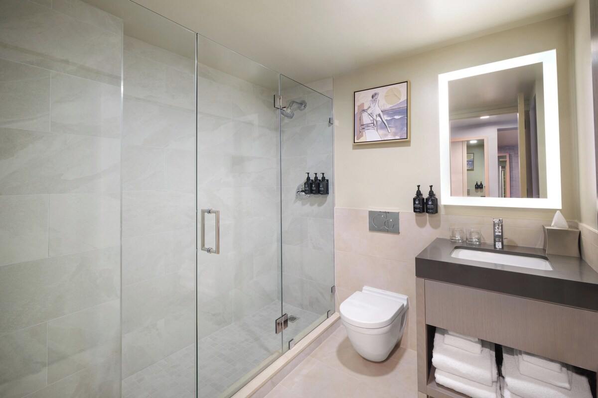 A modern bathroom with a glass-enclosed shower, a white toilet, and a vanity with a mirror.