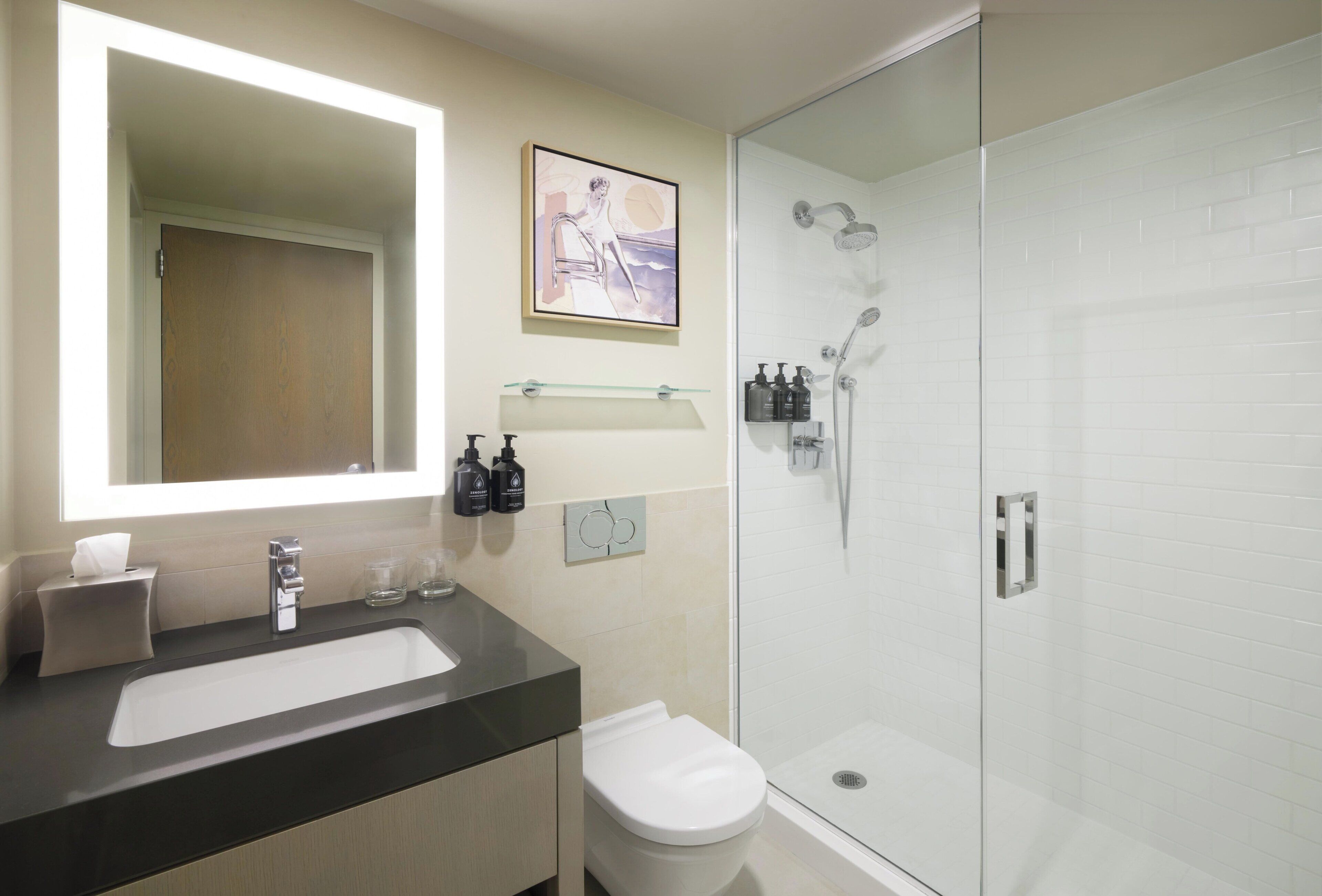 A modern bathroom with a large mirror, a white sink, a toilet, and a glass-enclosed shower.