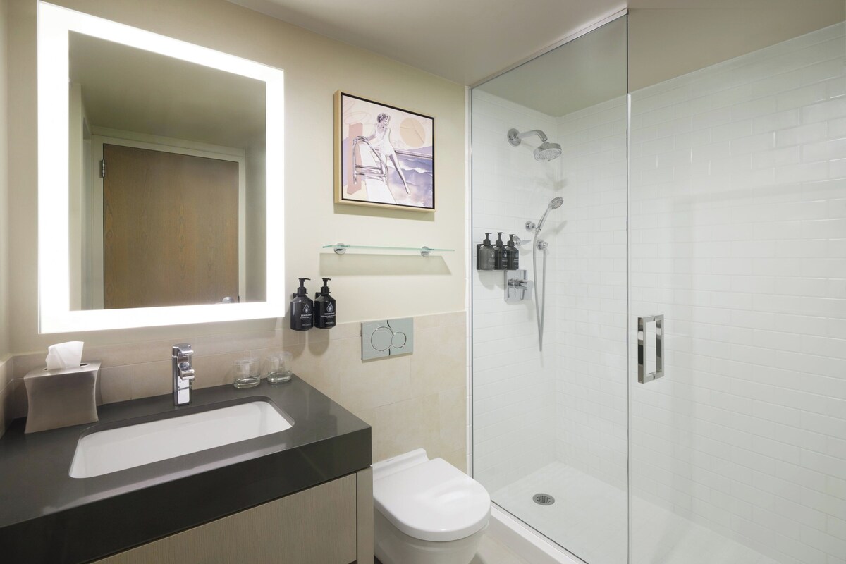 A modern bathroom with a large mirror, a white sink, a toilet, and a glass-enclosed shower.