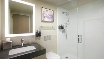 A modern bathroom with a large mirror, a white sink, a toilet, and a glass-enclosed shower.