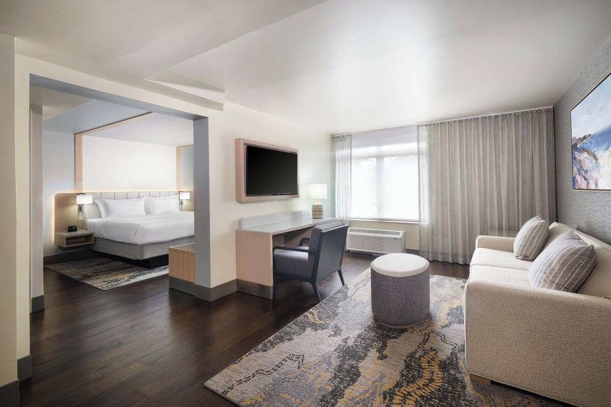 A hotel room with a bed, desk, TV, and a sofa.