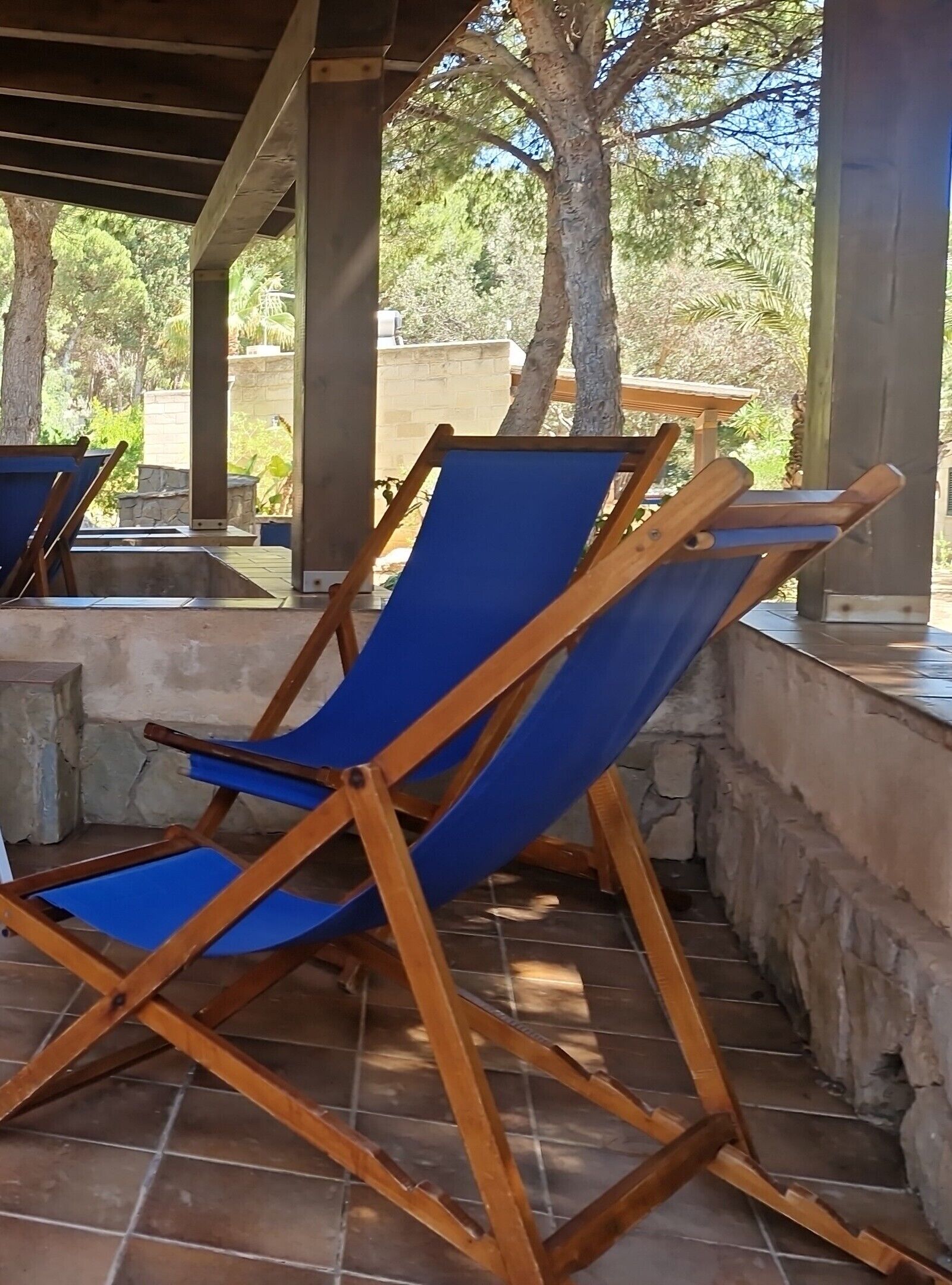 A covered outdoor seating area with wooden chairs and a blue canvas backdrop.