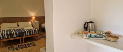 A hotel room with a bed, bedside table, lamp, and a tray with cups and a kettle.