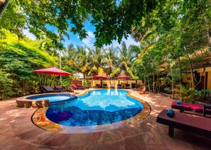 A swimming pool surrounded by lush greenery and red umbrellas. - Pavillon Indochine (Siem Reap)