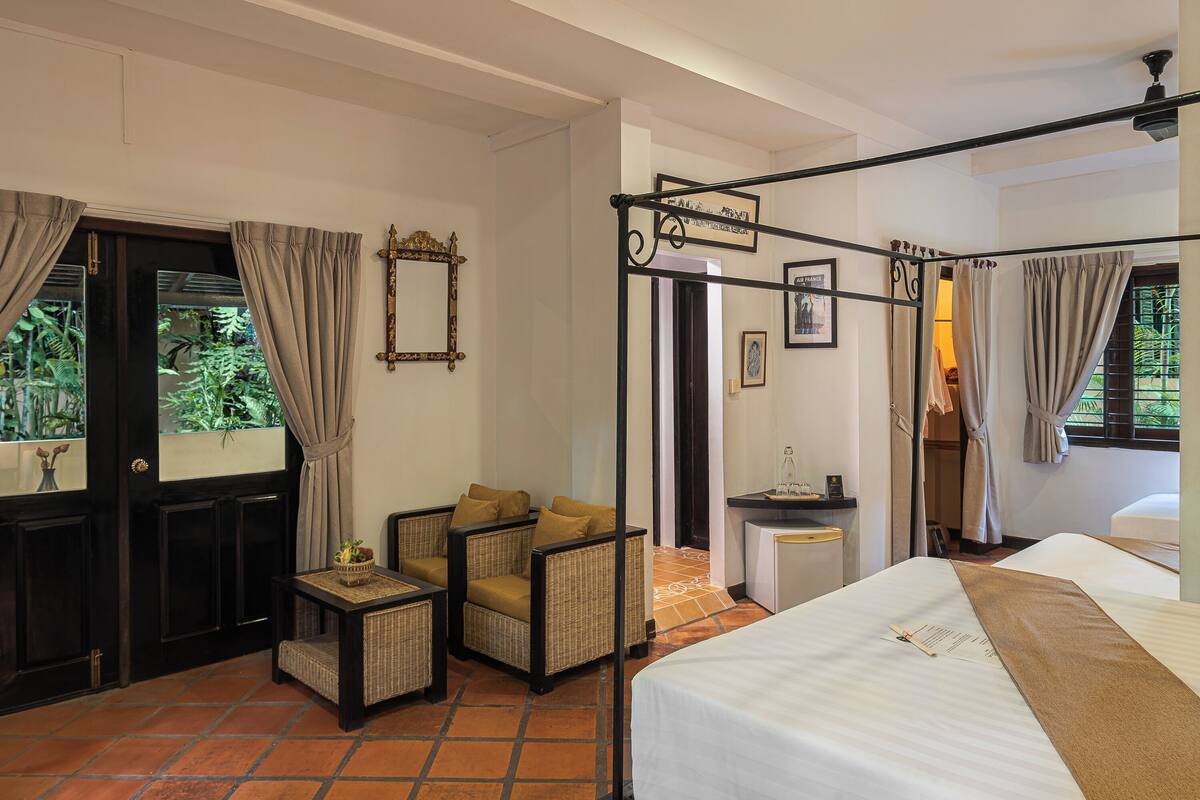 A hotel room with a bed, a chair, a small table, a mirror, and a window with curtains.