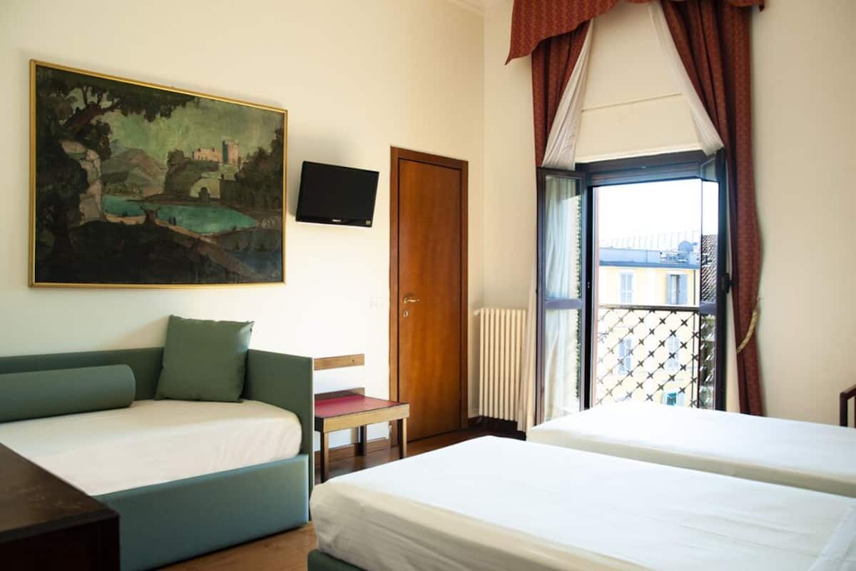 A hotel room with a bed, a sofa, a TV, a painting, and a window with a view.
