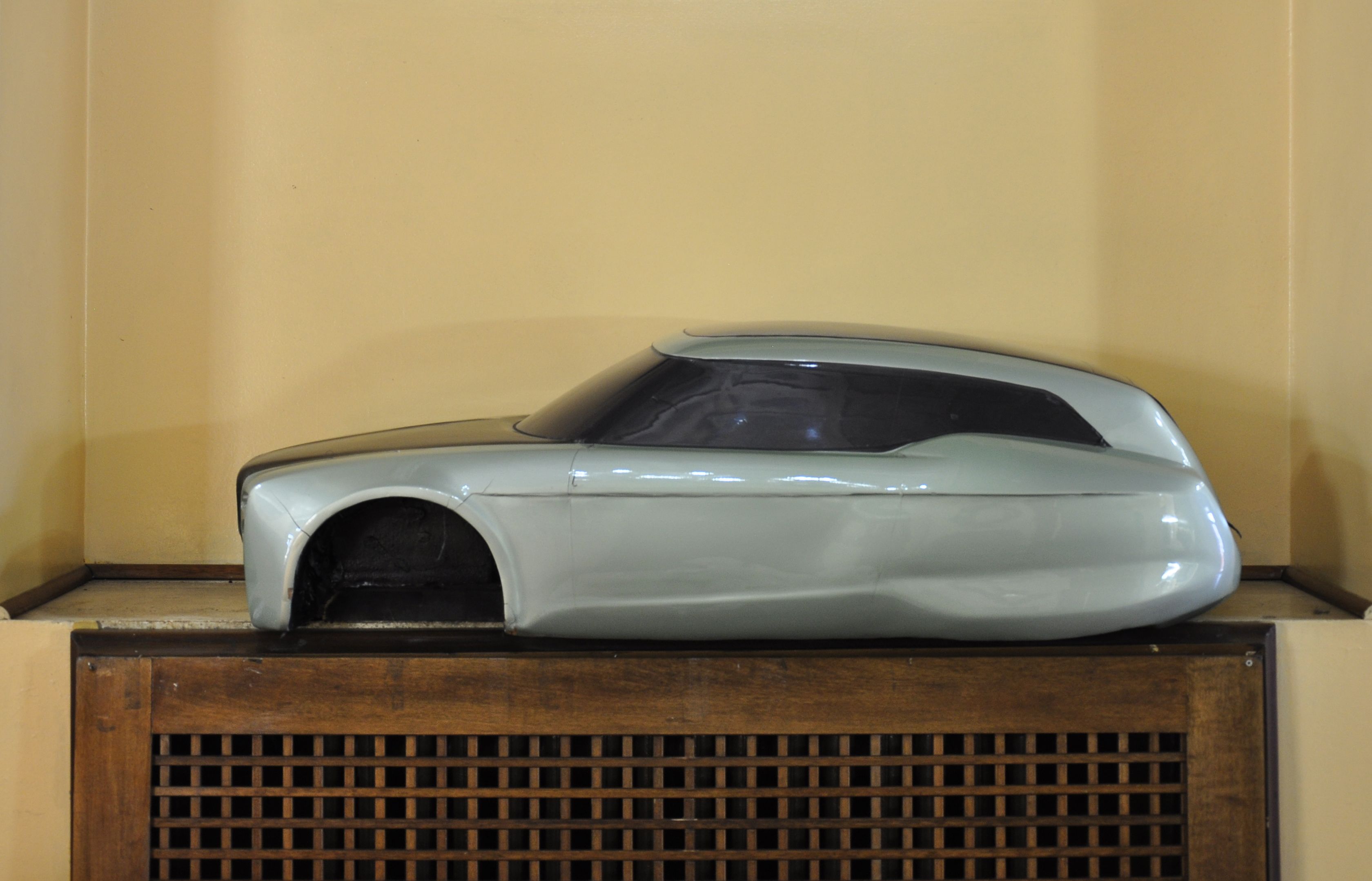 A model car displayed on a wooden stand against a plain wall.