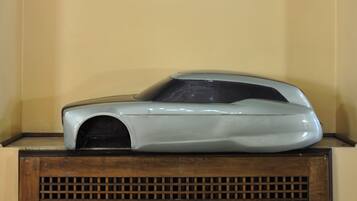 A model car displayed on a wooden stand against a plain wall.