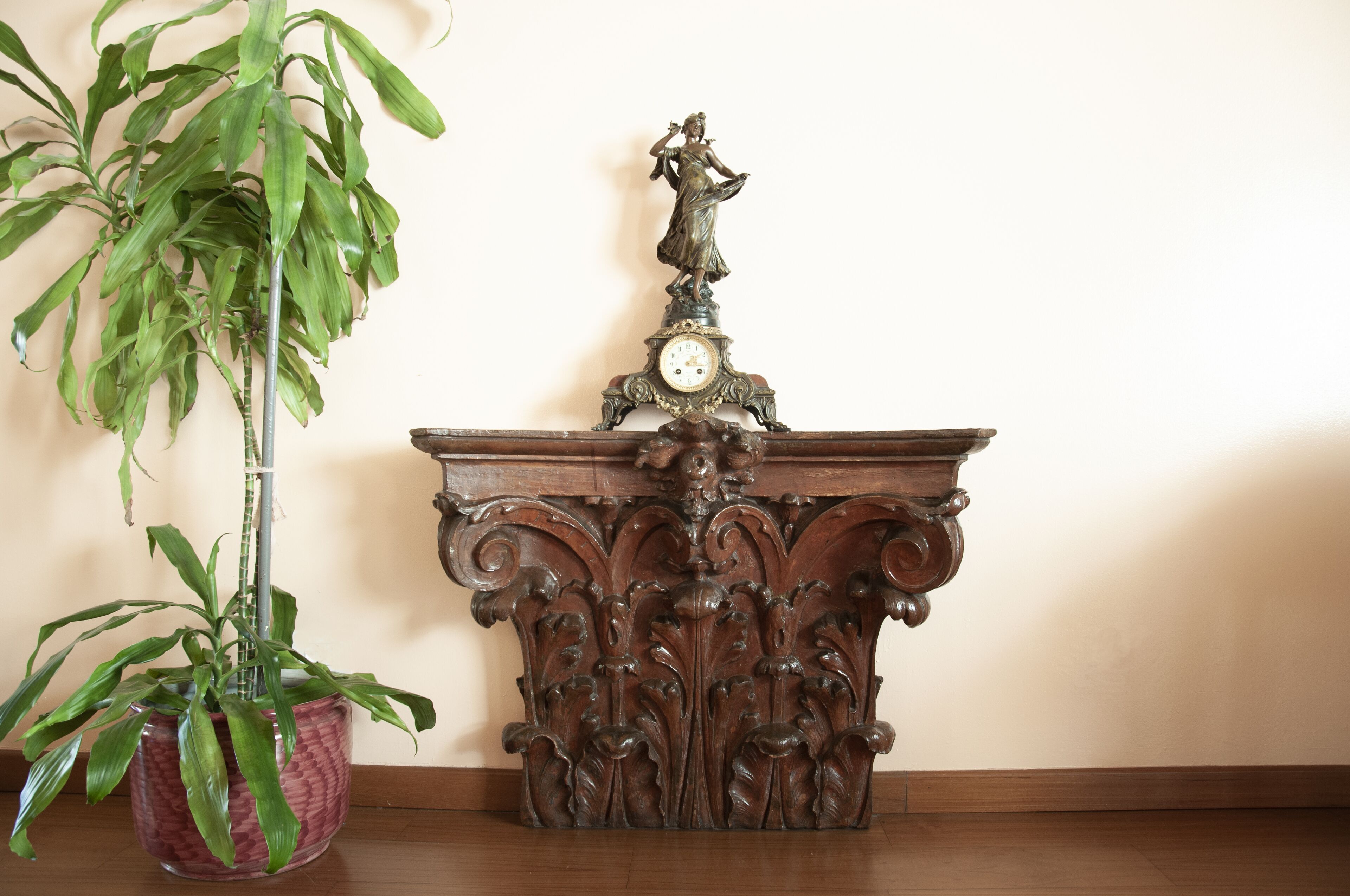 Een houten tafel met een versierde klok en een beeldje erop, naast een potplant.