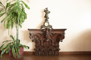 Een houten tafel met een versierde klok en een beeldje erop, naast een potplant.