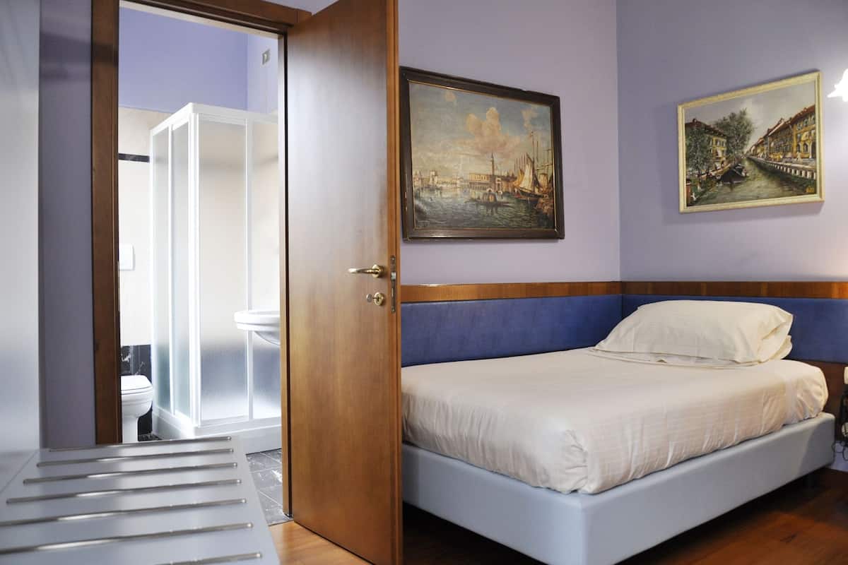 A bedroom with a bed, a door, a painting, and a view of a bathroom.