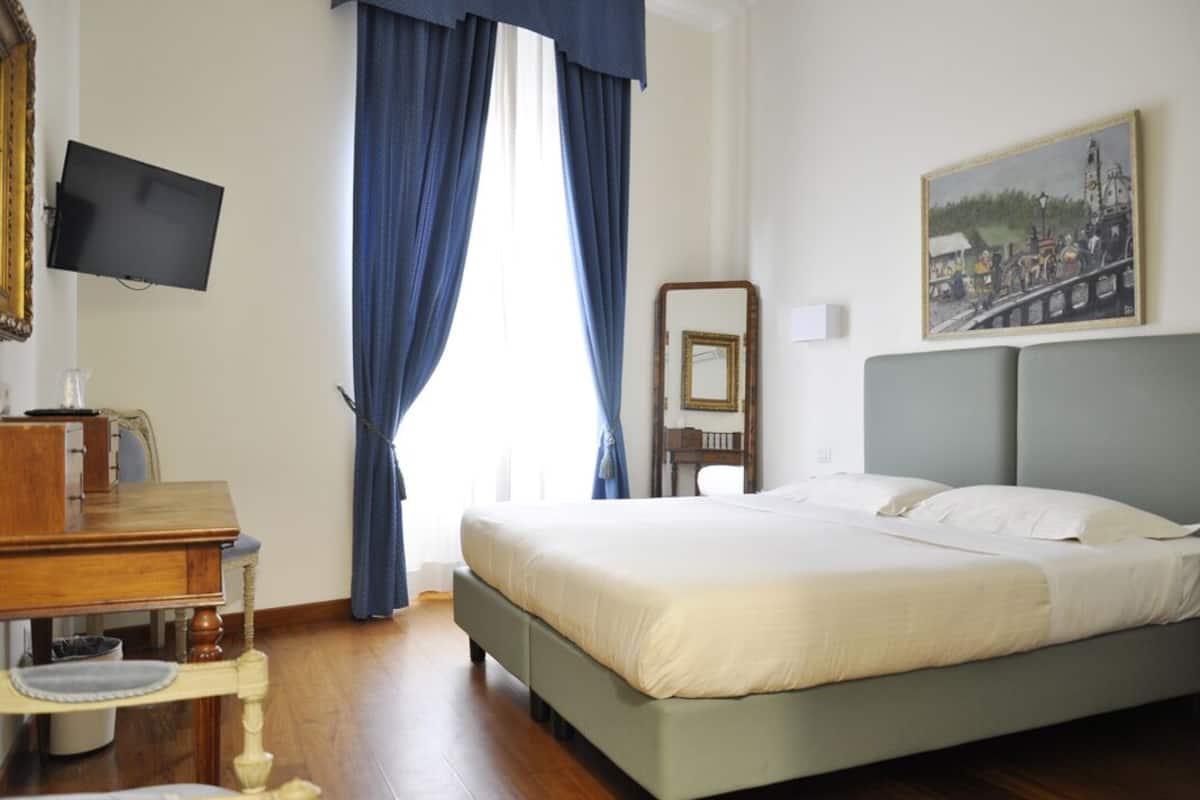 A hotel room with a bed, a desk, a television, and a painting on the wall.