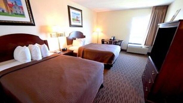 A hotel room with two beds, a desk, a chair, and a television. - Capri Motel (Mackinaw City)