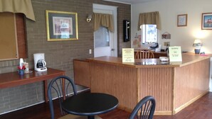 A small, cozy hotel room with a wooden reception desk, a coffee maker, and a dining area with a table and chairs. - Capri Motel (Mackinaw City)