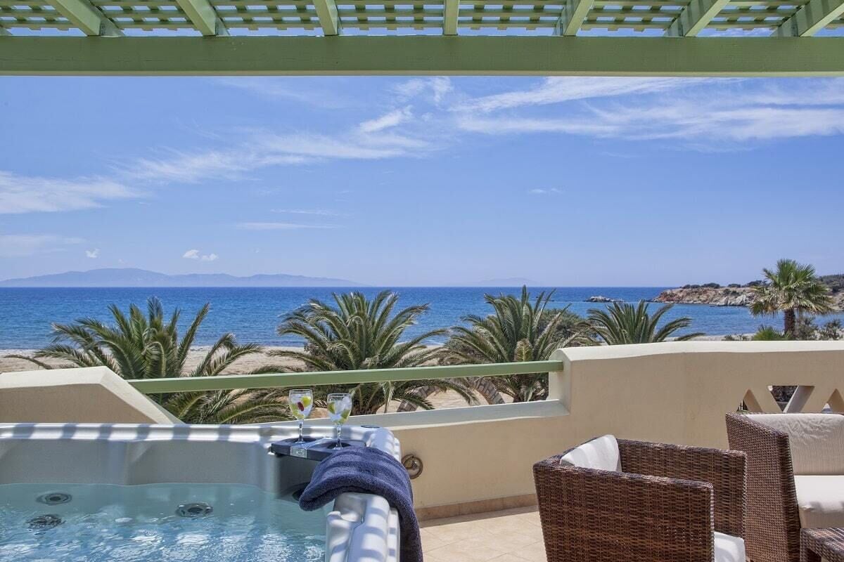 A balcony with a hot tub, wicker chairs, and a view of the beach and ocean.