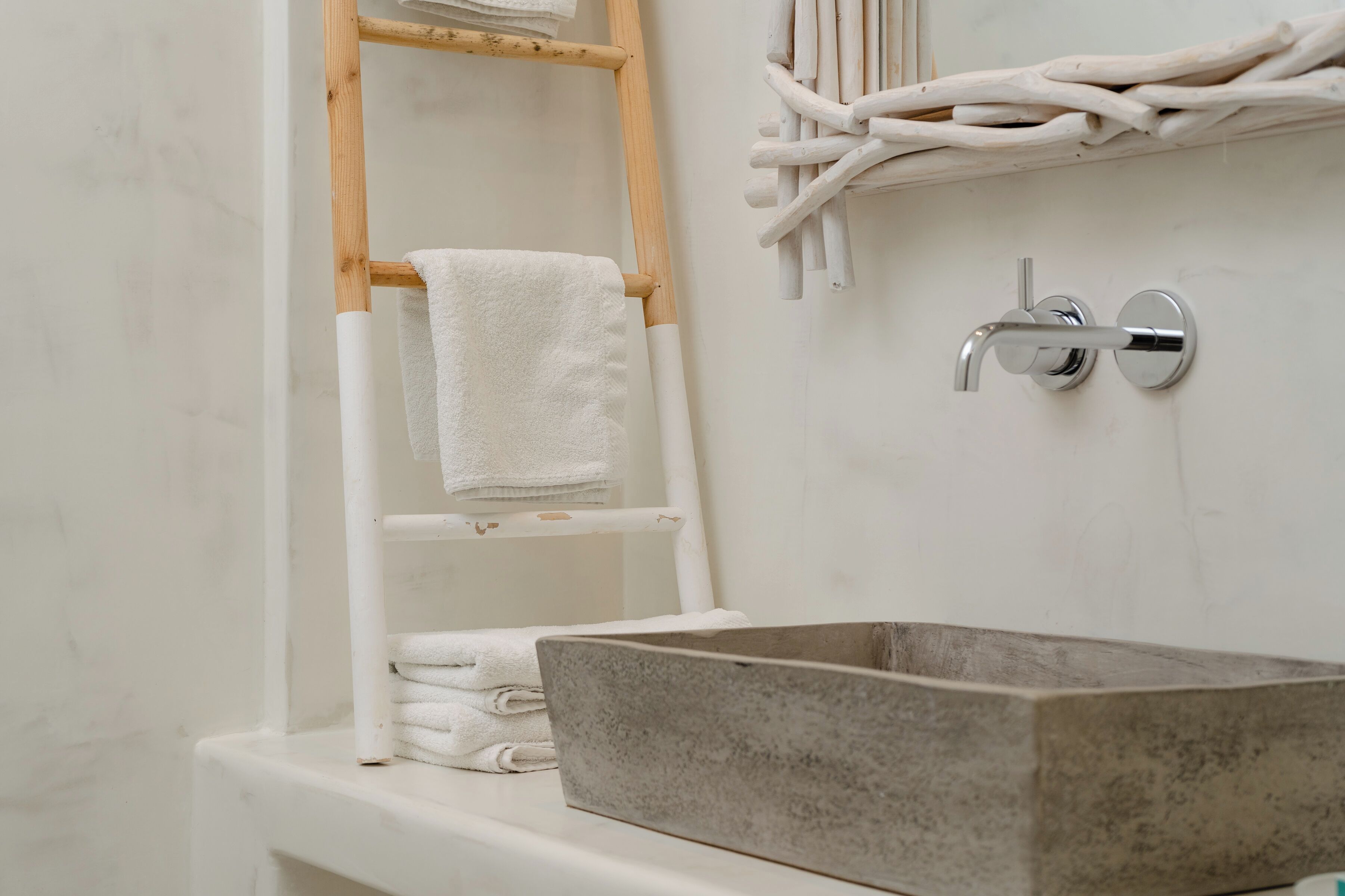 A bathroom with a wooden towel rack, a white shelf, and a large rectangular basin.