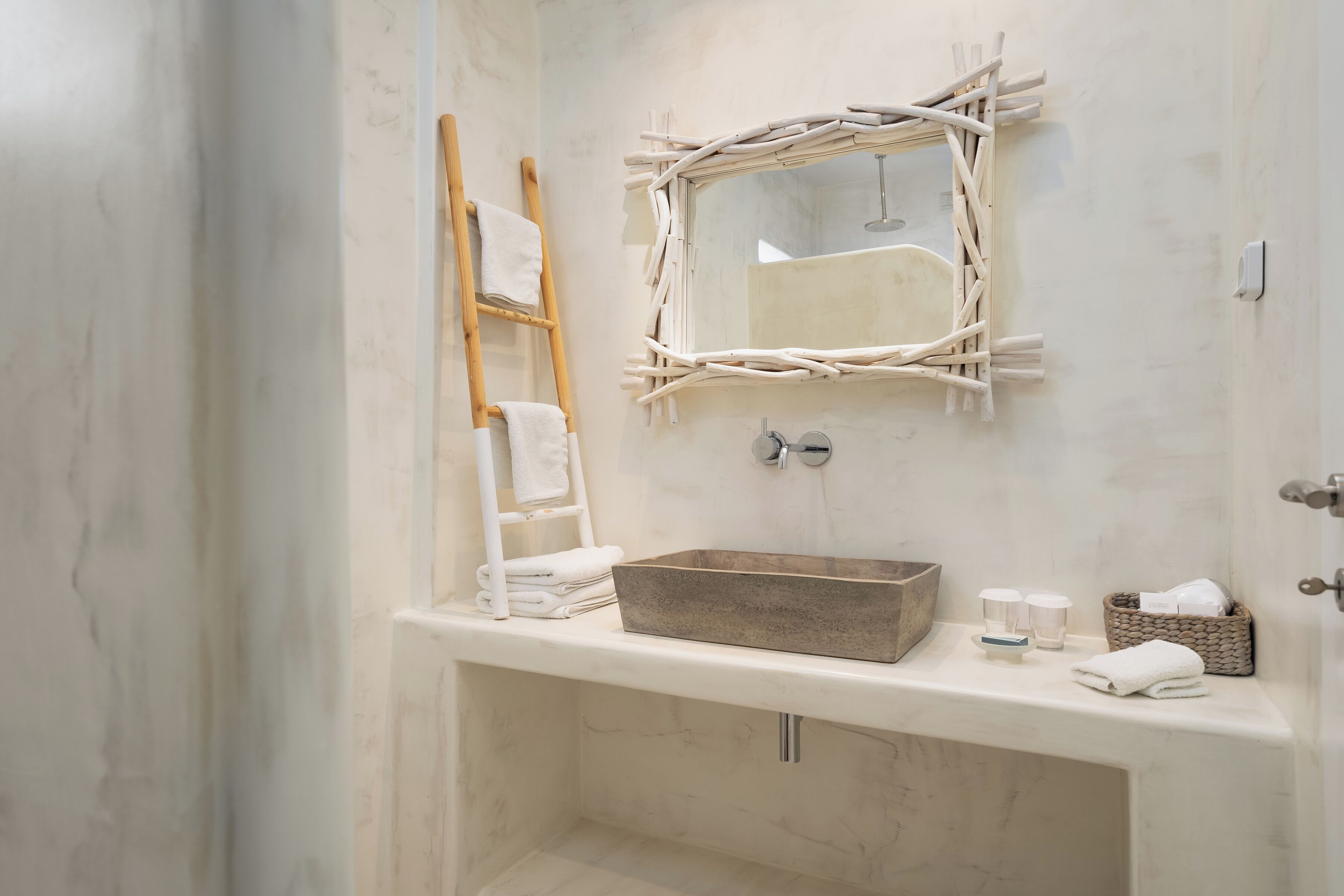 A bathroom with a marble sink, a wooden ladder, a mirror with a twig frame, and a towel rack.