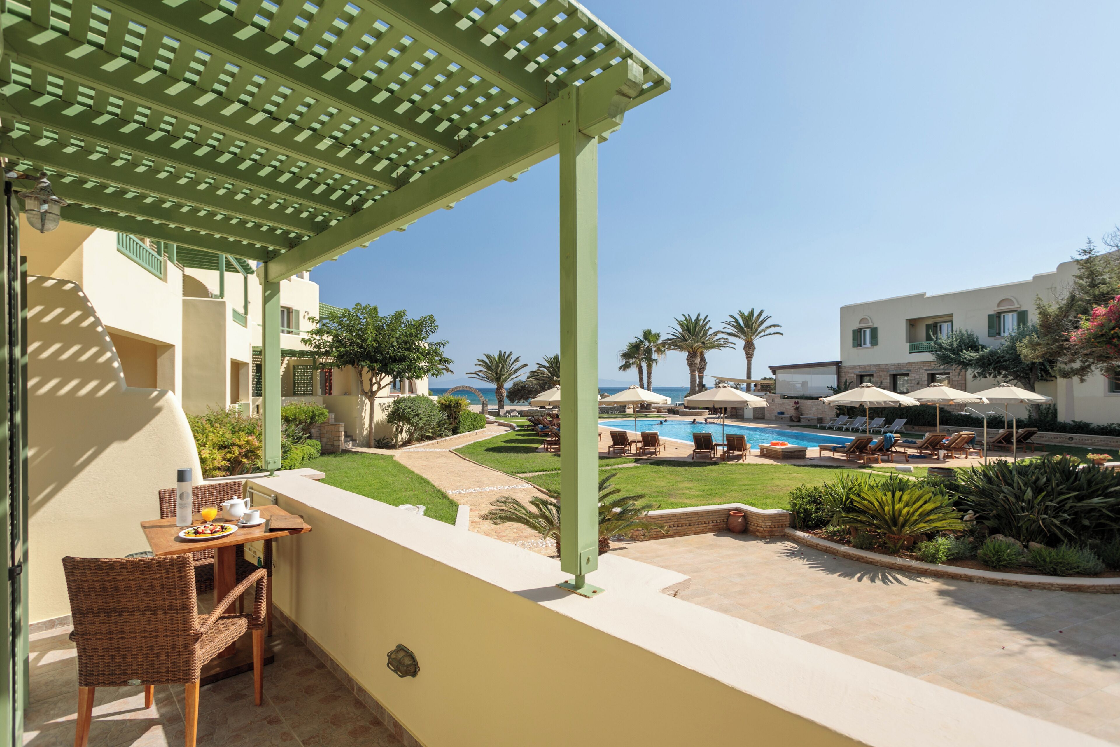 A balcony with a table, chairs, and a view of a pool area with umbrellas and lounge chairs.