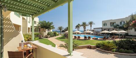 A balcony with a table, chairs, and a view of a pool area with umbrellas and lounge chairs.