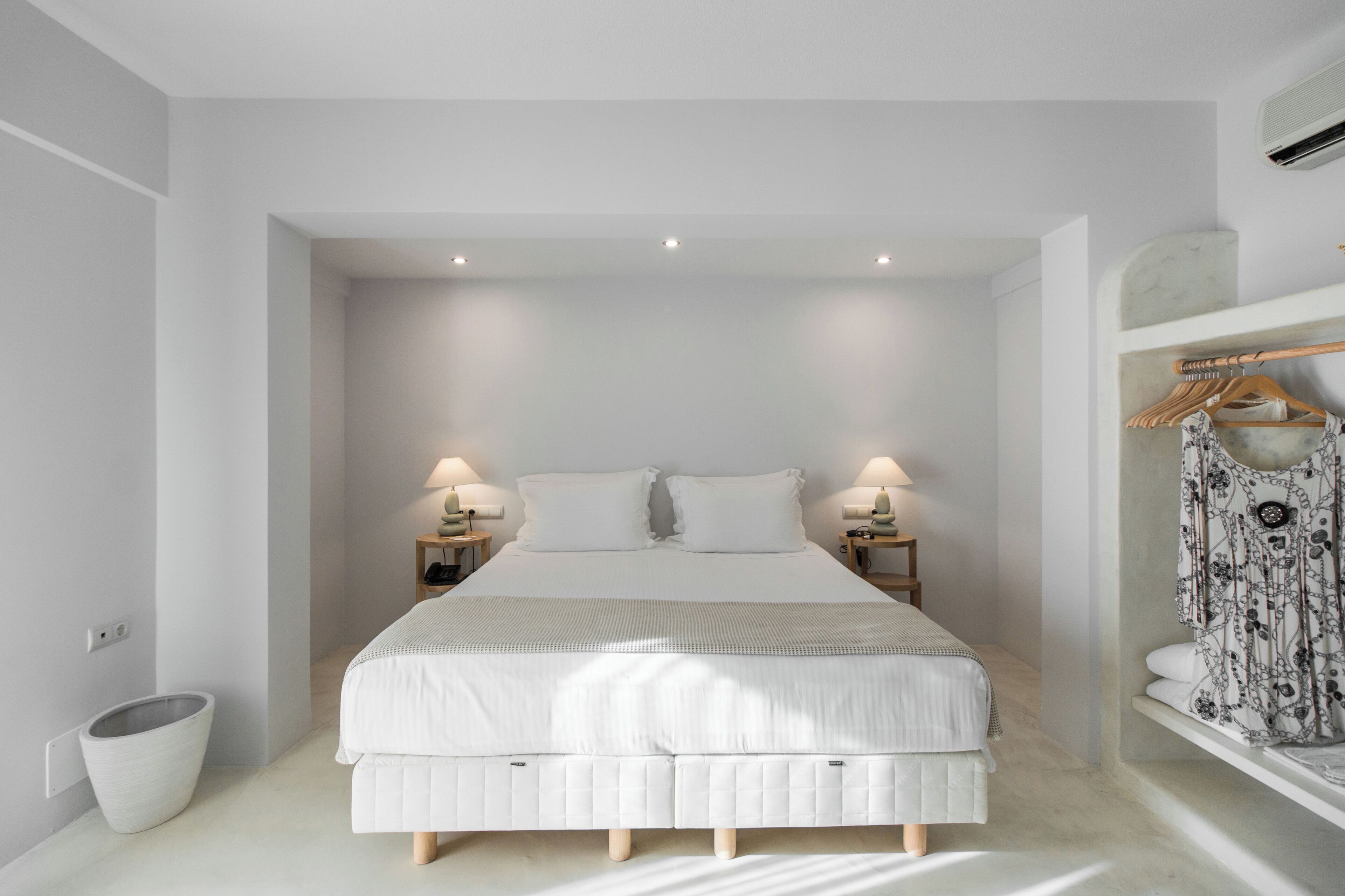 A modern bedroom with a large bed, bedside tables, a hanging wardrobe, and a small trash bin.