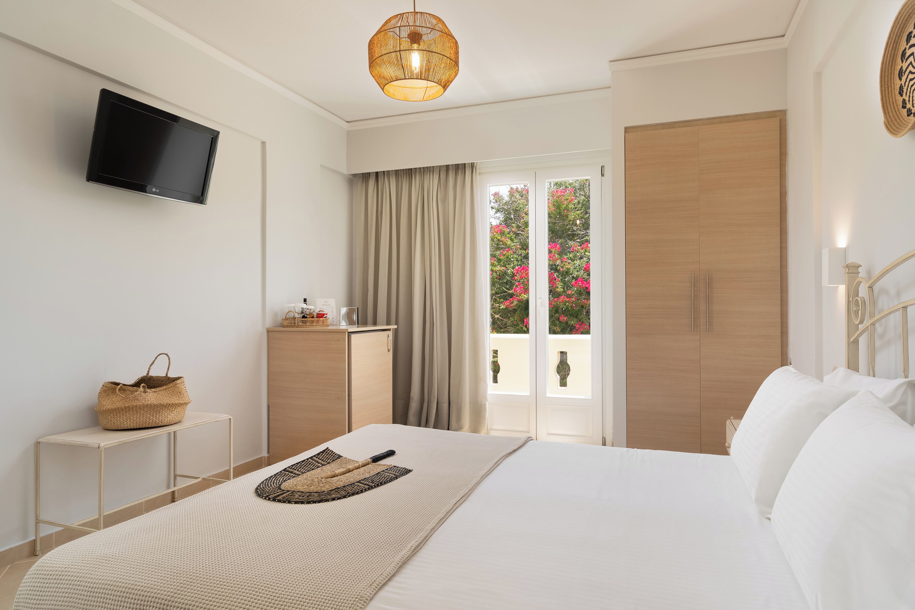 A hotel room with a bed, a television, a desk, a wardrobe, and a view of the outside.