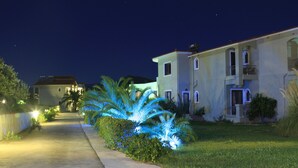 A residential street at night with houses on either side, a well-lit palm tree, and a clear sky. - Imerti Hotel (Lesvos)