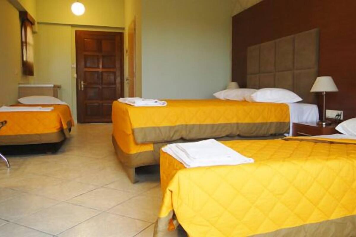 A hotel room with two beds, a wooden door, a nightstand, and a lamp.