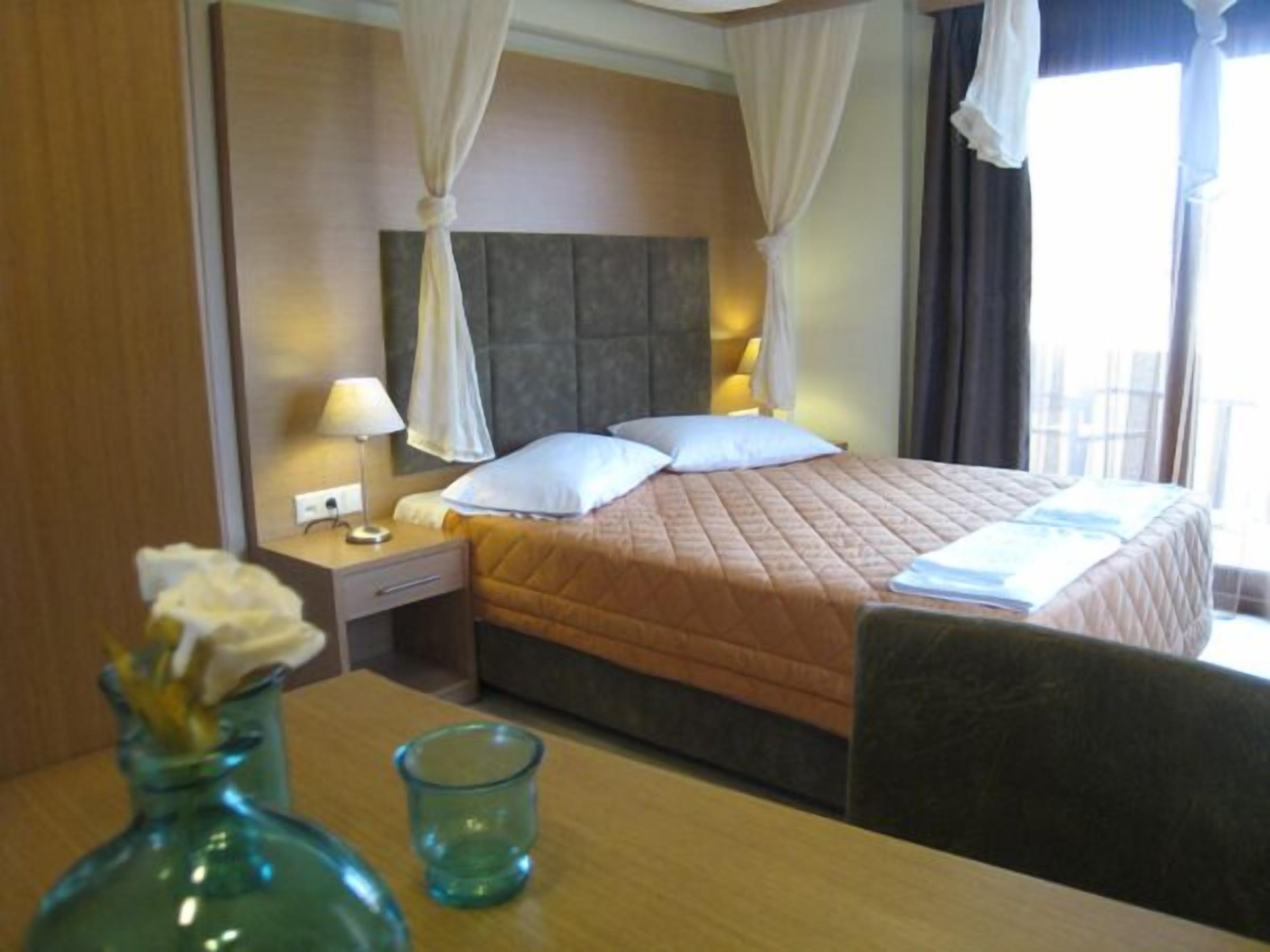 Una habitación de hotel con cama, mesita de noche, lámpara y un florero con flores.