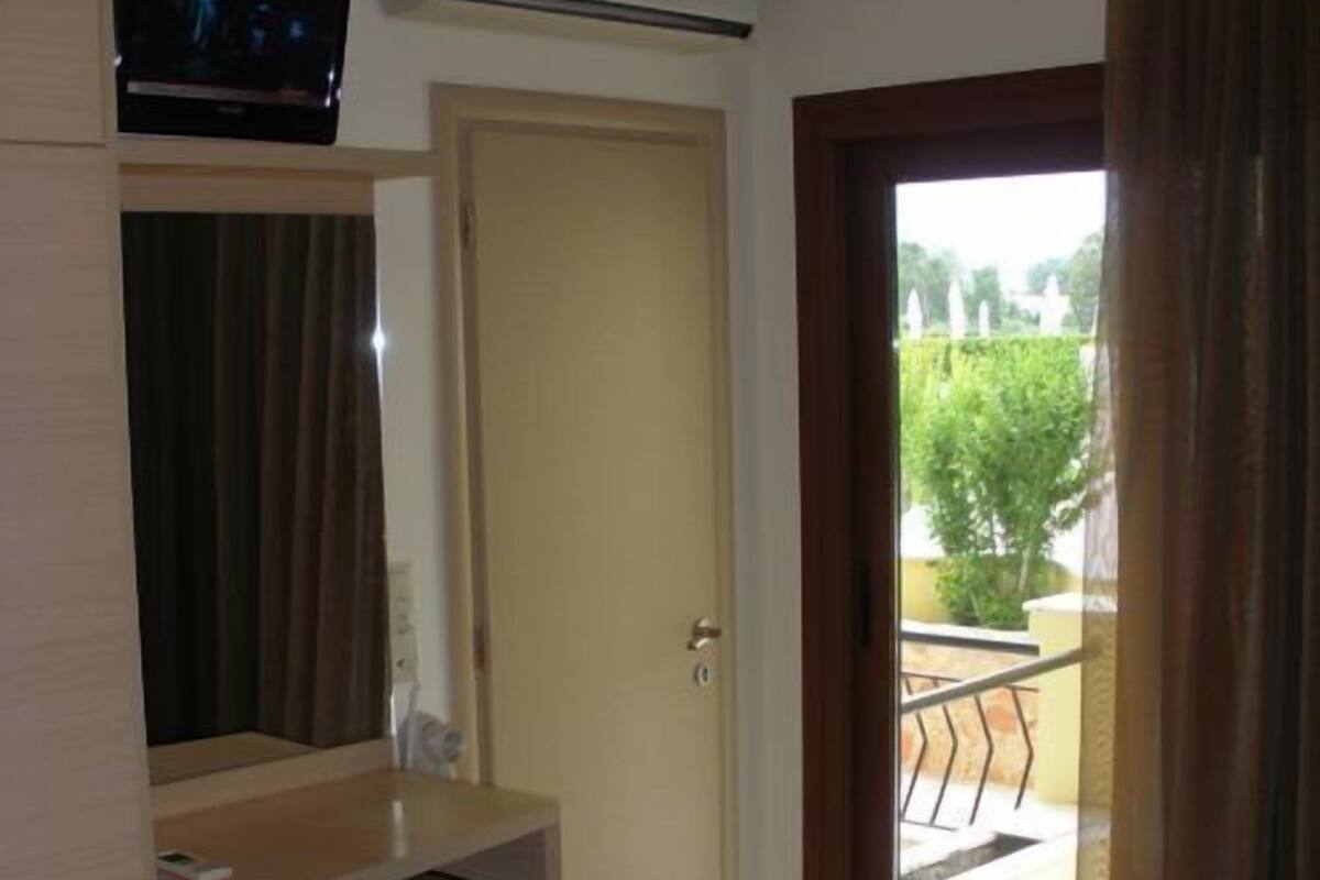 A hotel room with a desk, chair, bed, and a view of the outside.