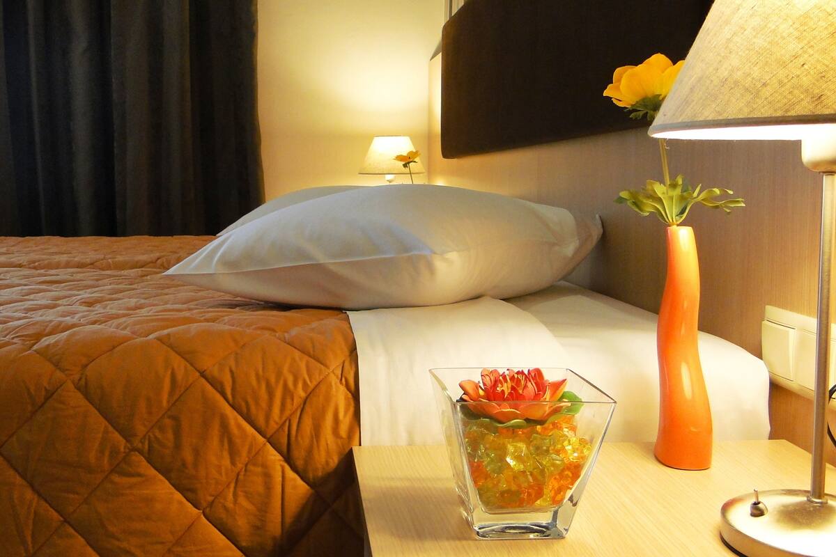 A hotel room with a bed, a nightstand, a lamp, and a vase with flowers.