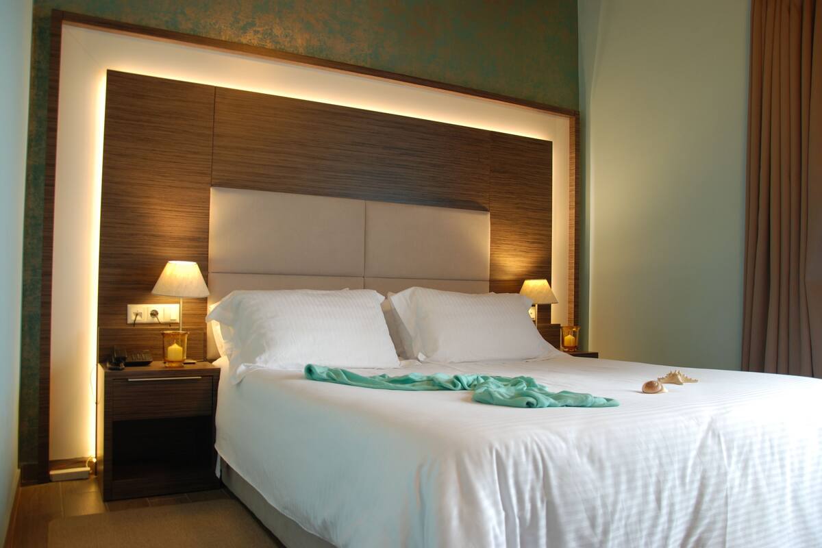 A hotel room with a large bed, two bedside lamps, and a nightstand with a lamp.