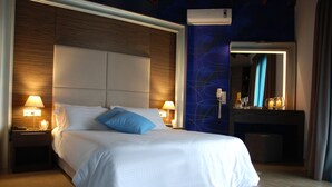 A hotel room with a large bed, two bedside lamps, a nightstand, a mirror, and a wall-mounted air conditioner. - Imerti Hotel (Lesvos)