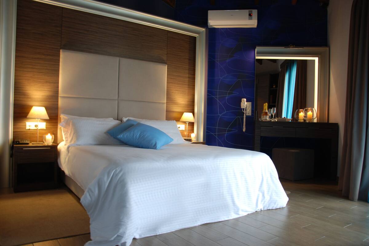 A hotel room with a large bed, two bedside lamps, a nightstand, a mirror, and a wall-mounted air conditioner.