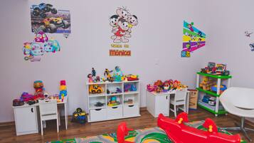 Un cuarto de juegos infantil con un escritorio blanco, estanterías llenas de juguetes y un tapete de juego colorido.