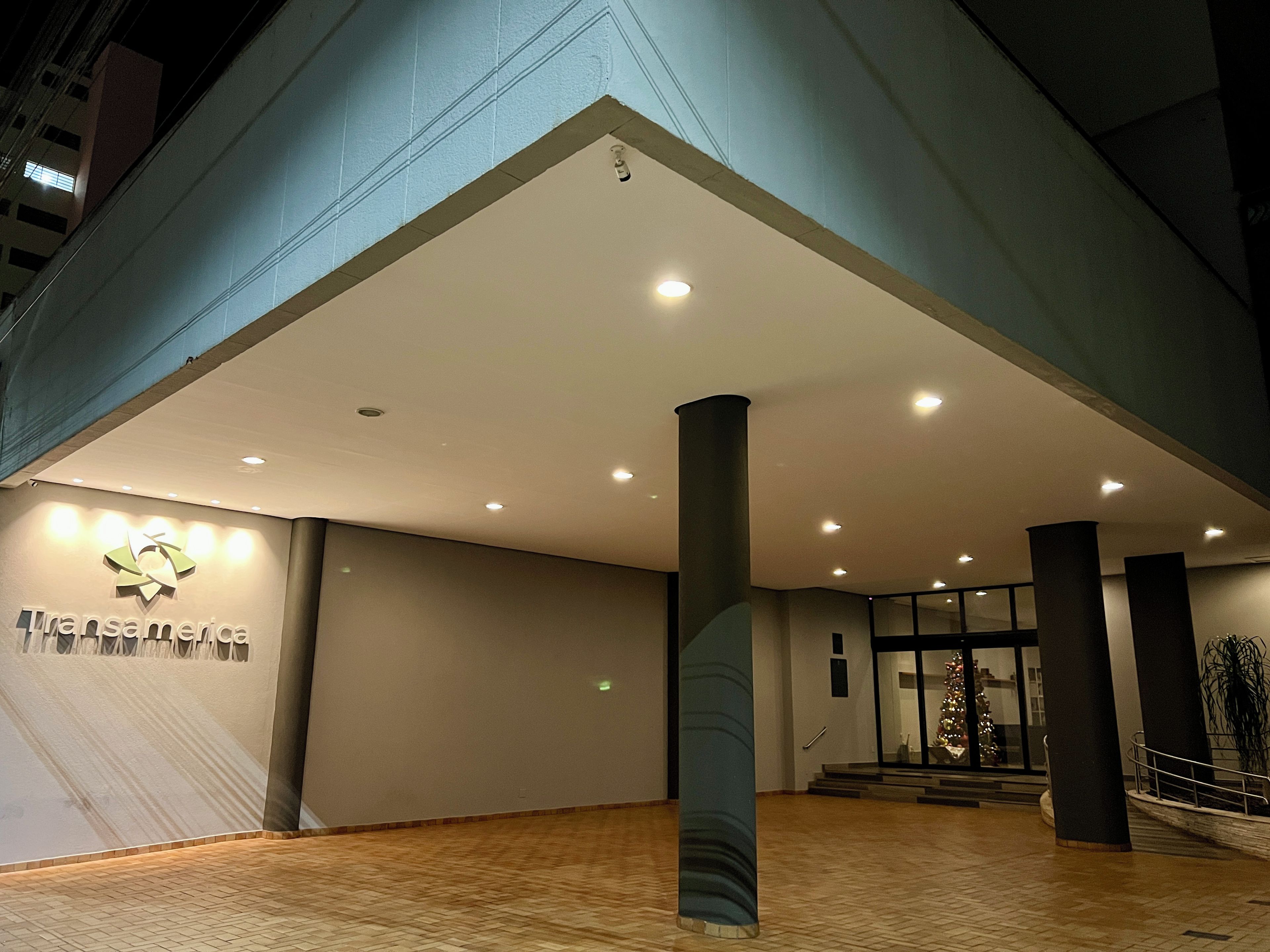 Entrada de um edifício moderno com um logotipo, uma escadaria e um pinheiro de Natal.
